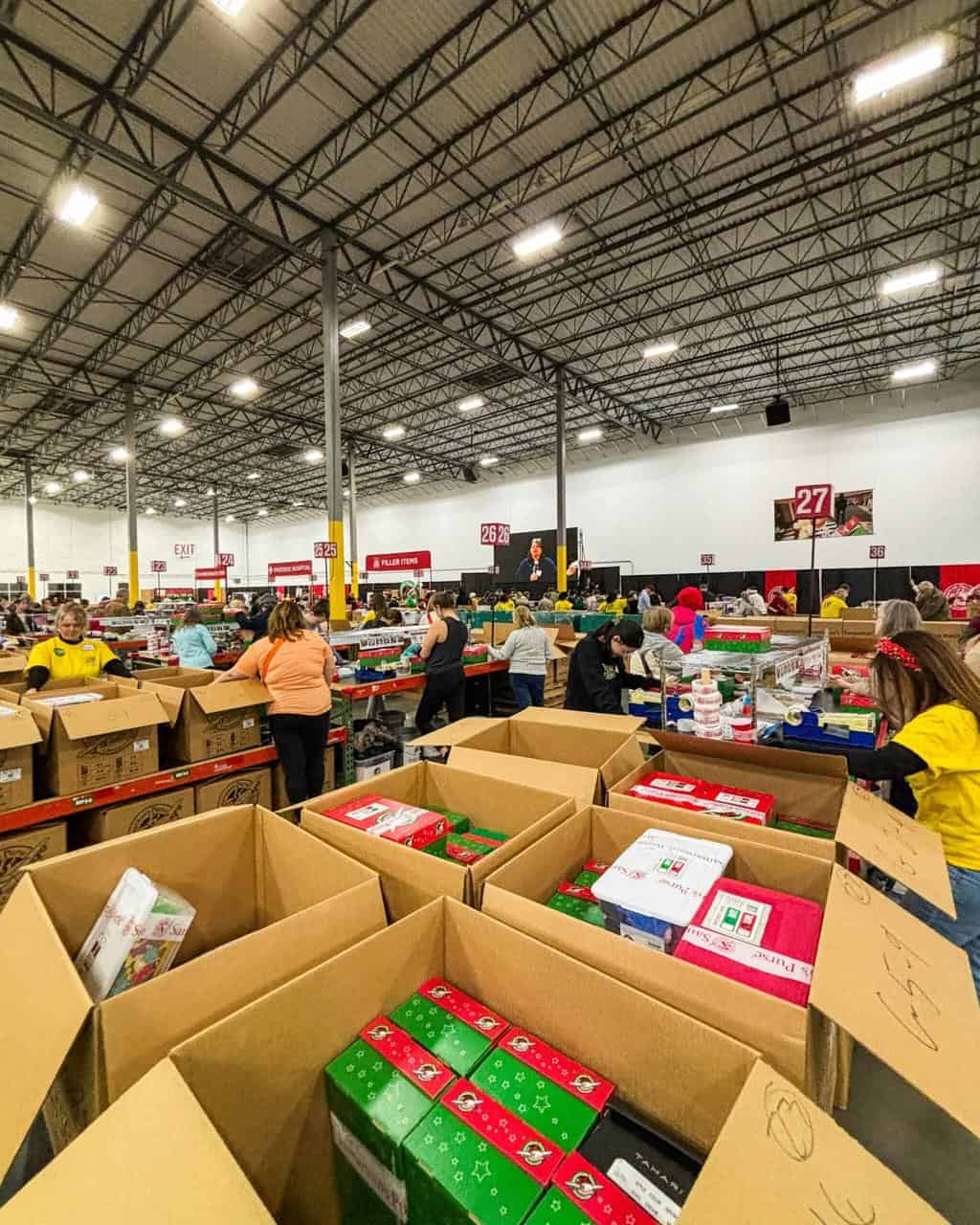 Volunteers sorting gift boxes in a large warehouse during a community outreach event.