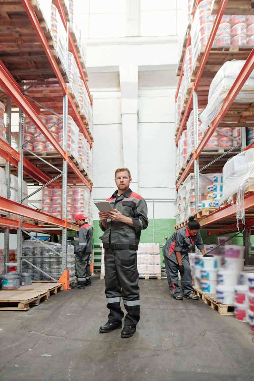Warehouse supervisor overseeing inventory with tablet among stocked shelves