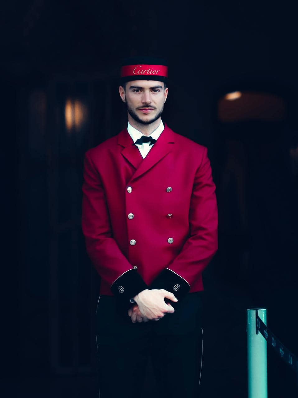 Hotel bellhop in formal red uniform standing at an entrance—representing front-of-house hospitality and entry-level service roles.