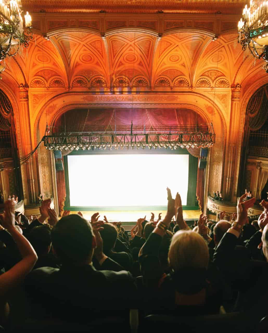 Audience applauding inside a grand cinema or theatre—representing careers in film projection, cinema operations, and live event support.