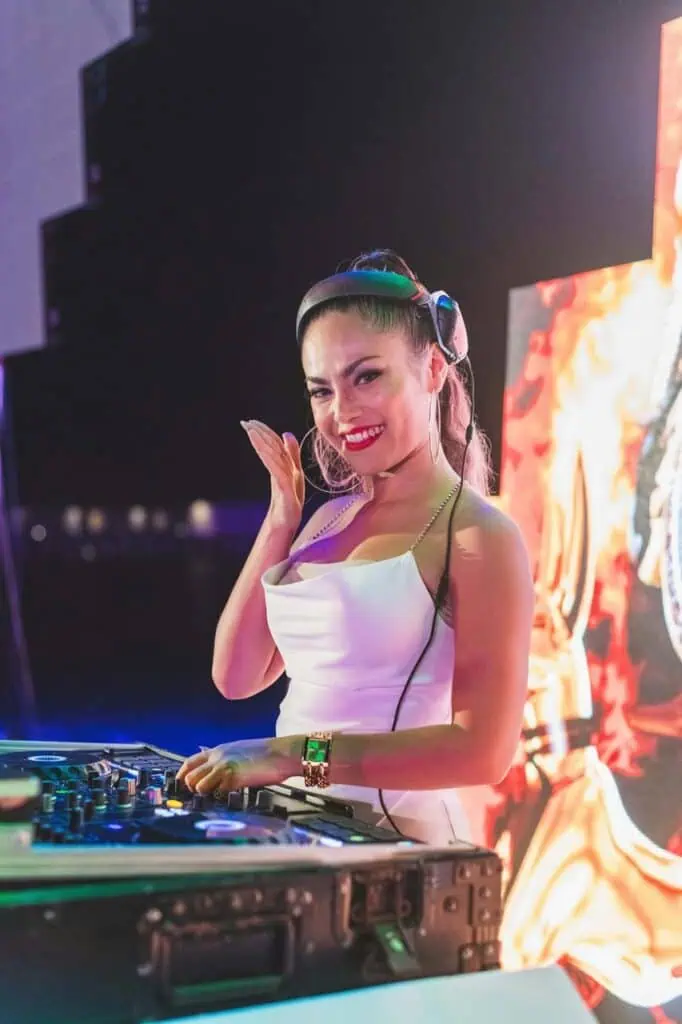 Female DJ in white dress performing at an event with a smile—representing careers in entertainment, music, and live audio production.