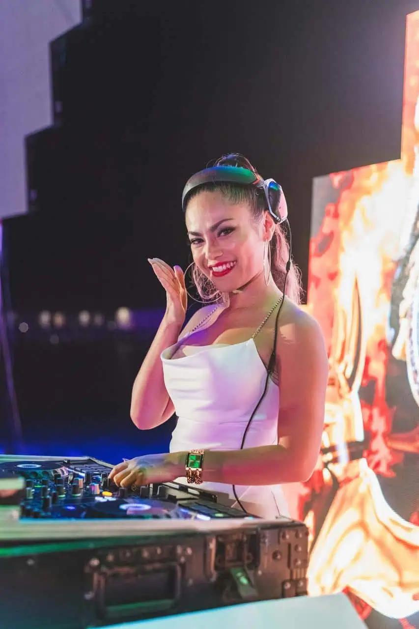 Female DJ in white dress performing at an event with a smile—representing careers in entertainment, music, and live audio production.