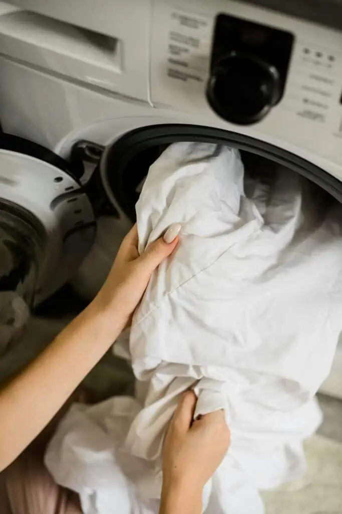 Hands placing white linen into a front-loading washing machine—representing laundry operations and linen supervisor roles in hospitality.