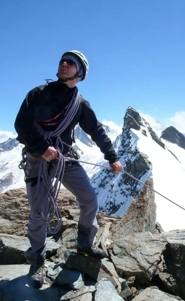 mountain climbing instructor securing rope on rocky summit with snowy peaks in background
