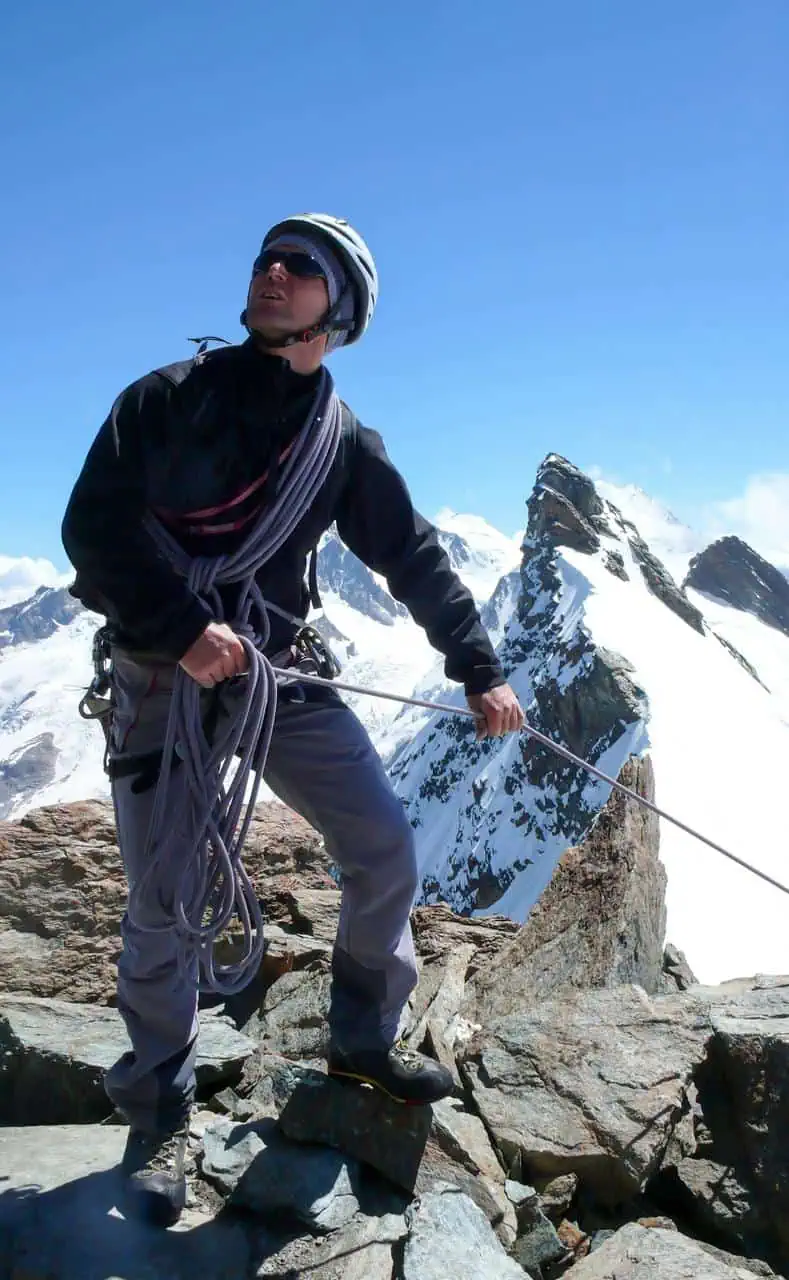 mountain climbing instructor securing rope on rocky summit with snowy peaks in background