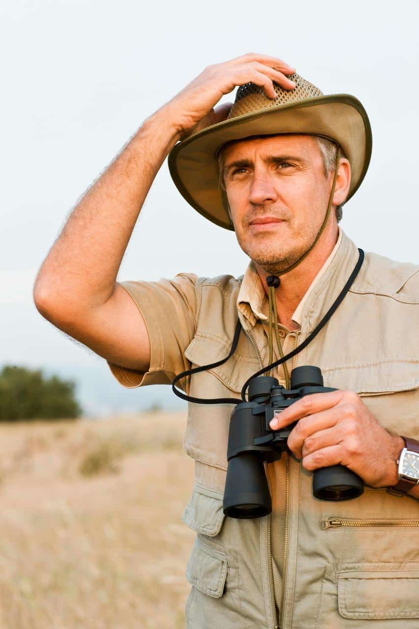 A national park ranger wearing a safari hat and holding binoculars, surveying the natural landscape during wildlife monitoring and conservation duties.