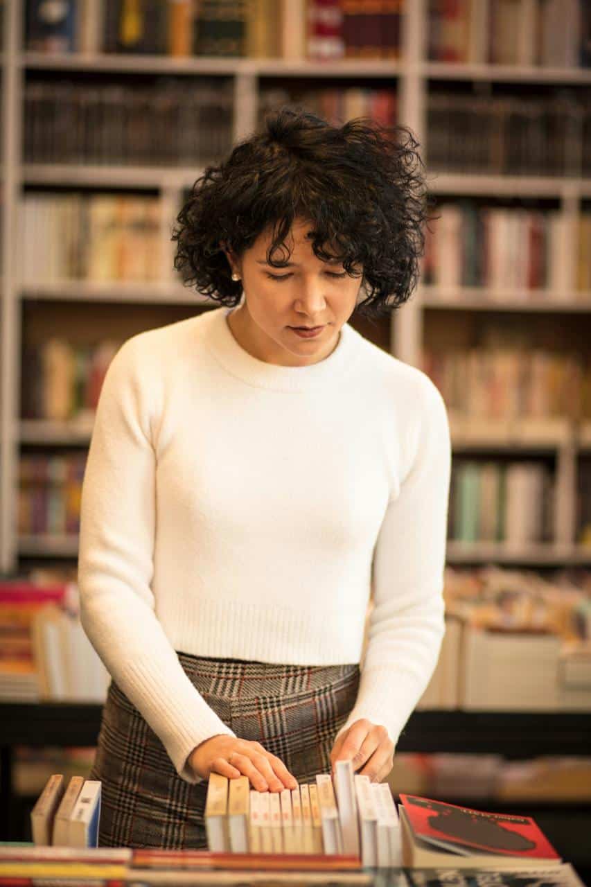 A professional public librarian in a white sweater organizing books on a library display table, focusing on community literacy.