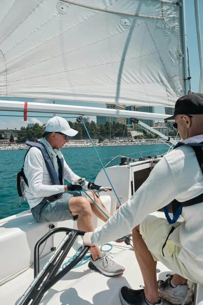 A sailing instructor guiding a student on a yacht near the shore, teaching maritime navigation and boating skills under clear skies.