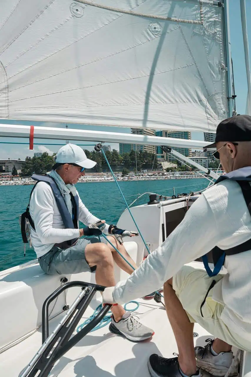 A sailing instructor guiding a student on a yacht near the shore, teaching maritime navigation and boating skills under clear skies.