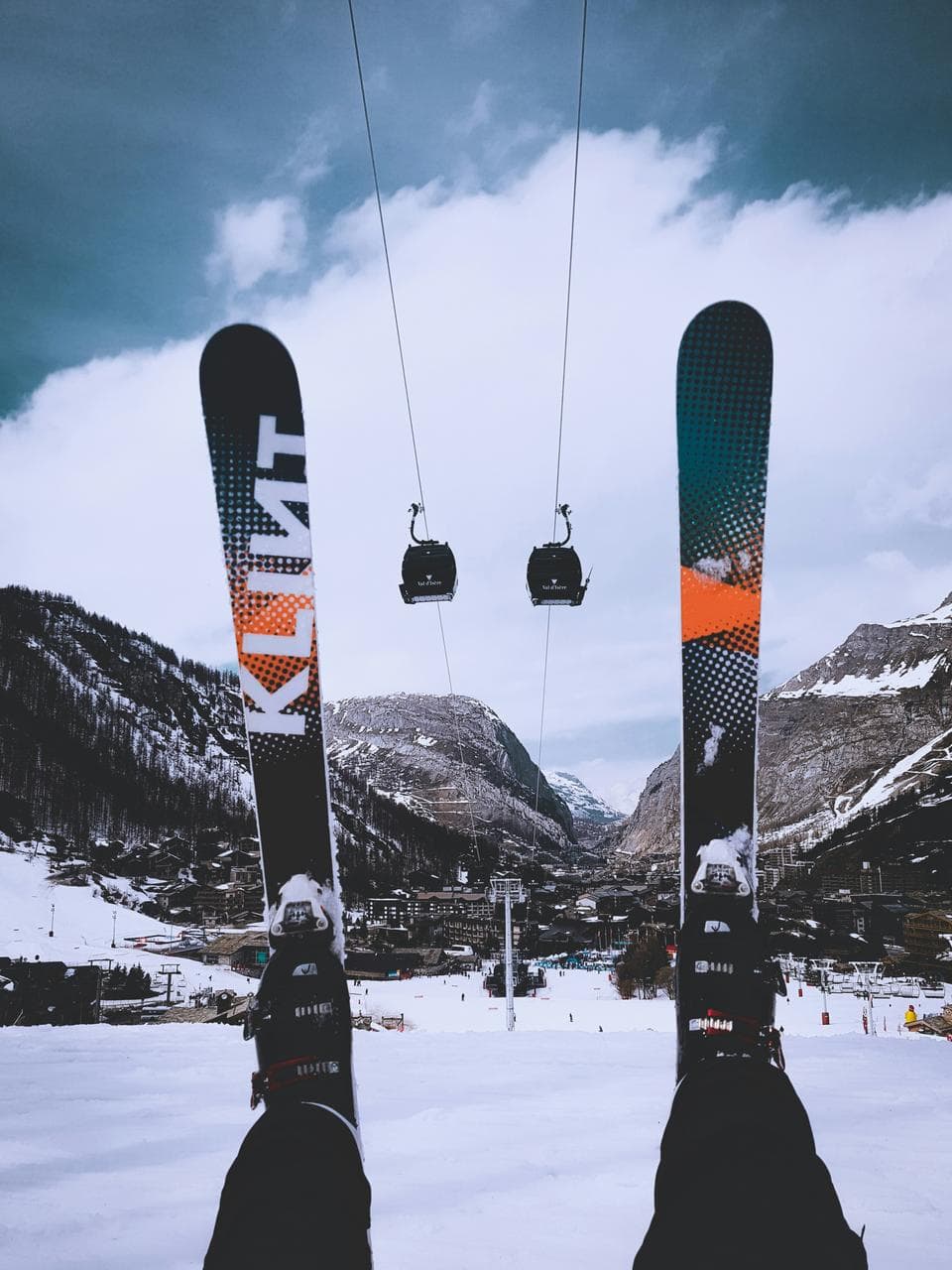 Ski instructor overlooking an alpine ski resort from the slopes, with skis lifted and cable cars in the background, preparing for a day of teaching students on the snow-covered mountains.
