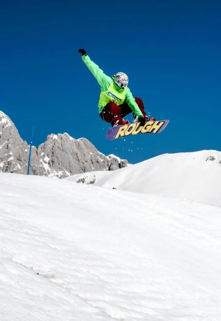 Snowboarding instructor performing a mid-air trick on a snowy mountain slope, teaching advanced freestyle techniques in a winter sports resort.