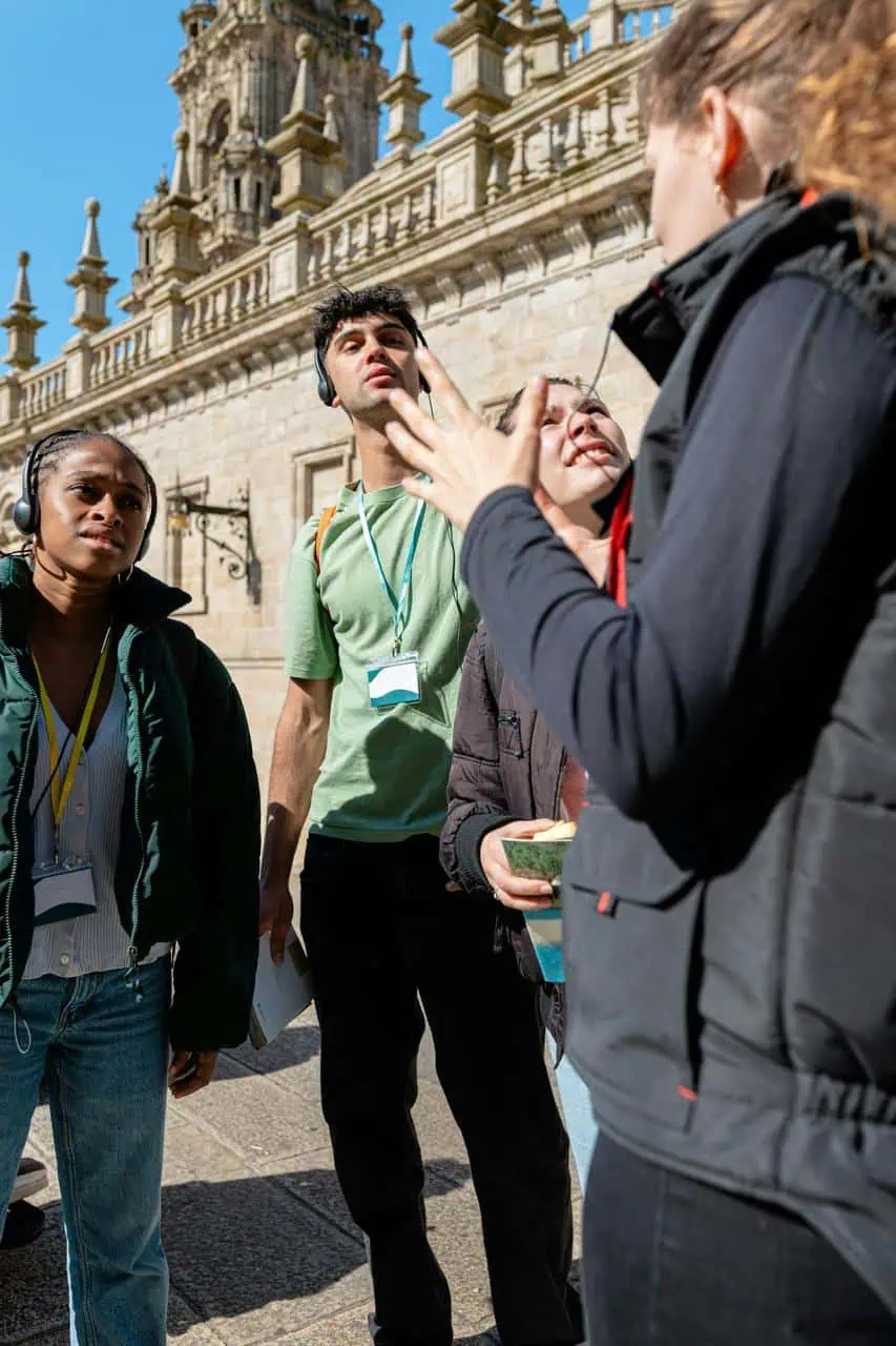 Tour guide leading a group of diverse tourists near a historic building, using hand gestures and headsets for clear communication and cultural education.