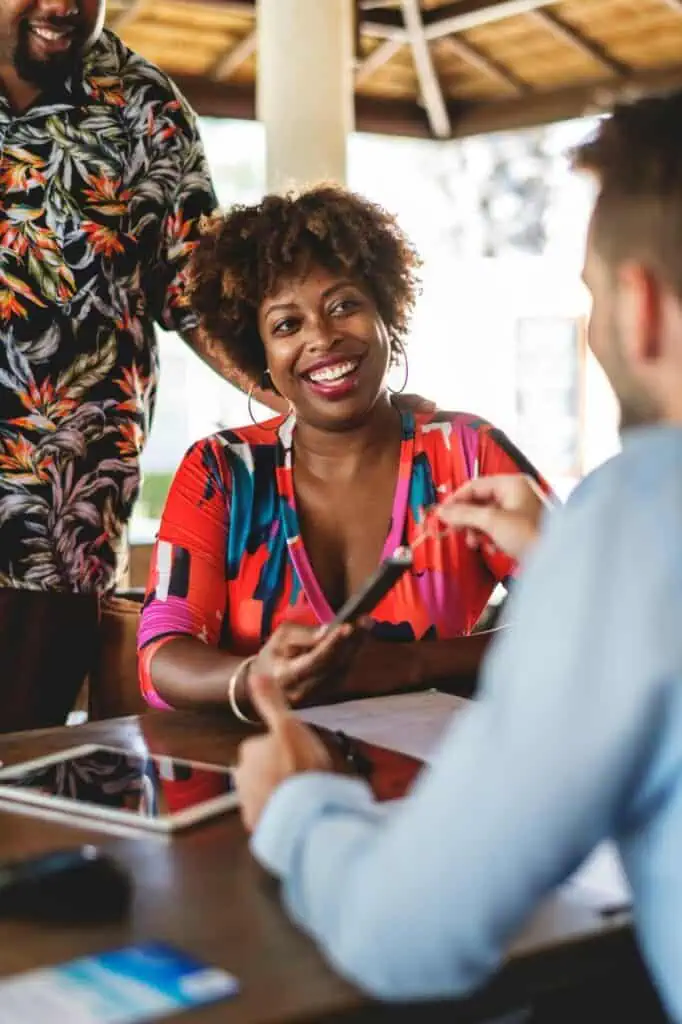 Smiling travel and tourism customer service representative assisting clients with vacation planning at a modern booking office.
