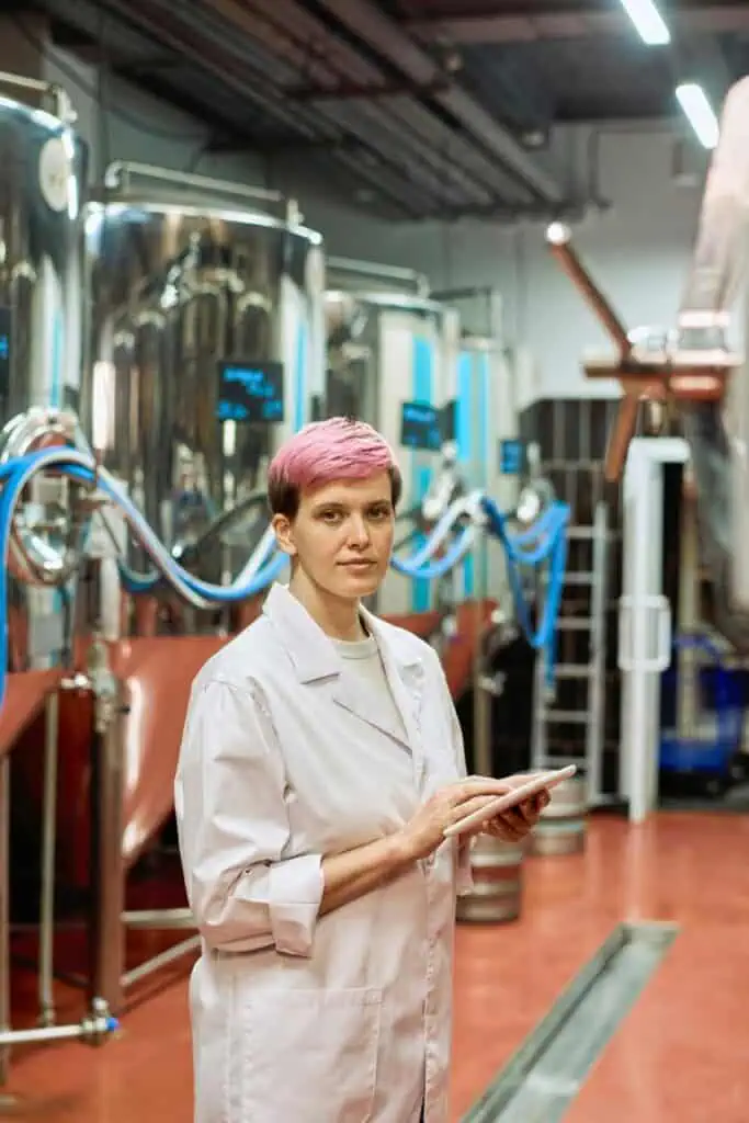 Female factory operations manager with tablet inspecting industrial brewing equipment