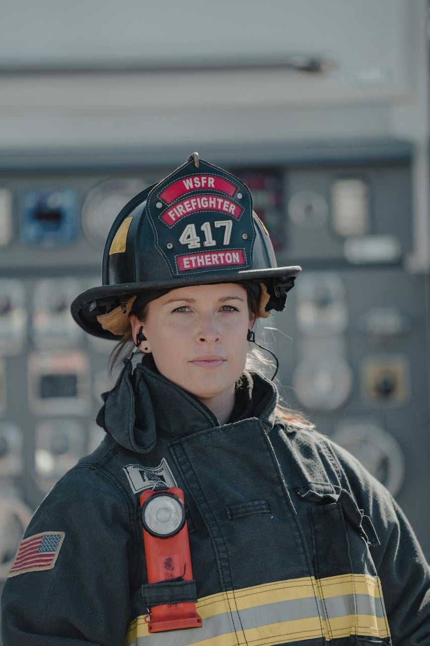 Female firefighter in uniform standing confidently at fire truck control panel