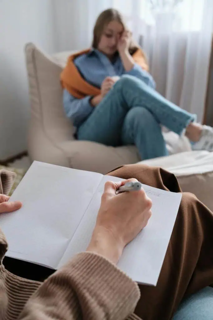  Licensed professional counselor taking notes during therapy session with distressed client