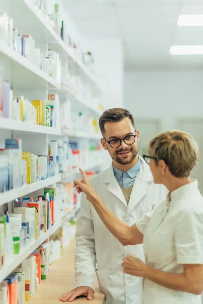 Pharmacist wearing glasses consulting with colleague about medication shelves in pharmacy