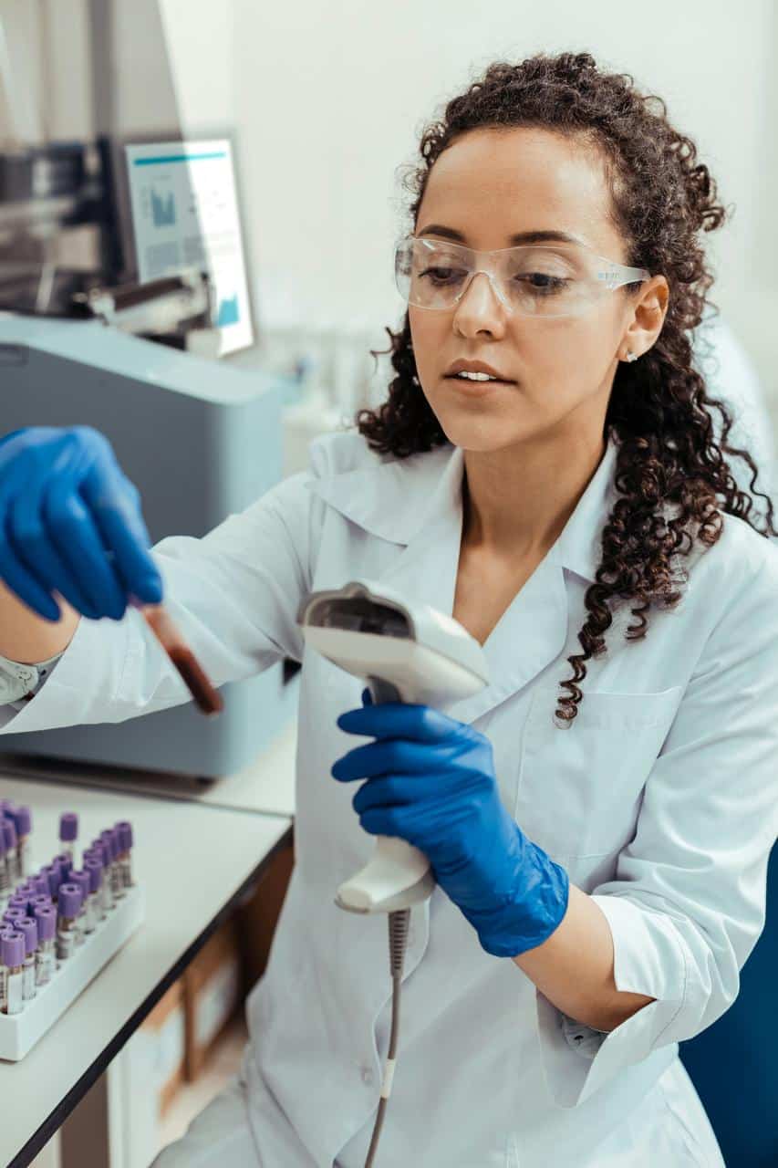 Phlebotomist wearing safety glasses preparing blood collection equipment in laboratory