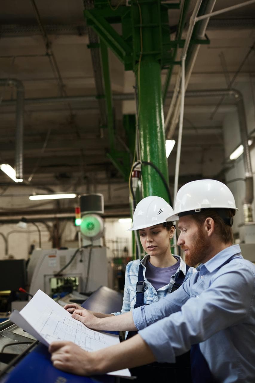 Production supervisor team reviewing blueprints wearing safety helmets in manufacturing facility