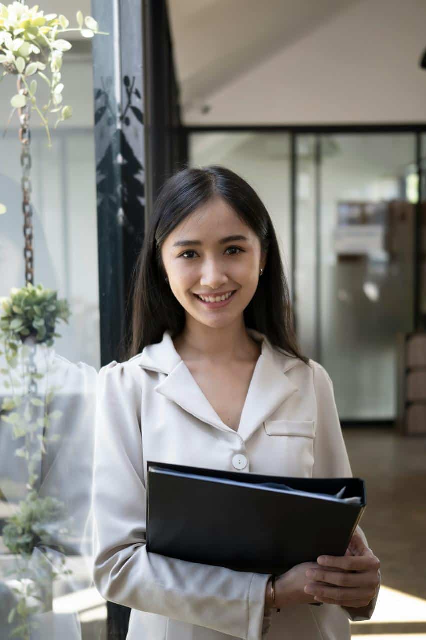Professional receptionist holding a folder and smiling at office front desk