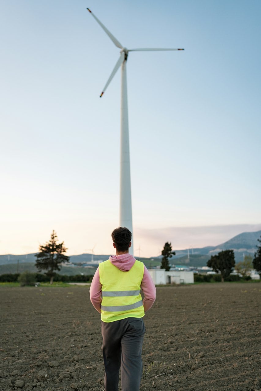 Renewable energy consultant surveying wind turbine installation site at sunset