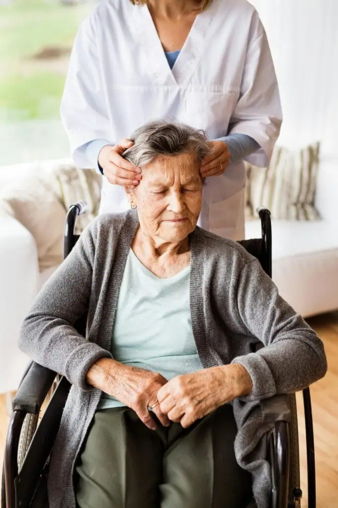 Rest home caregiver providing gentle head massage to elderly woman patient