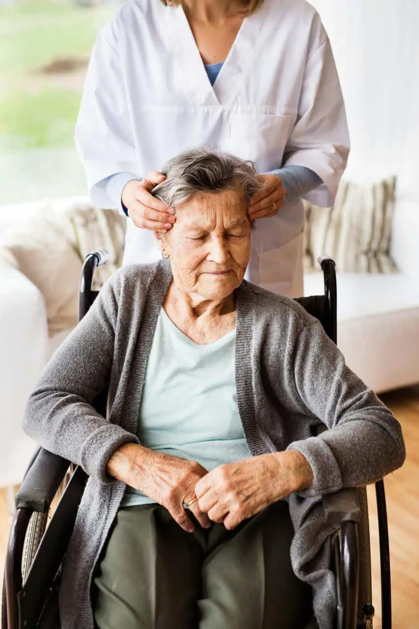 Rest home caregiver providing gentle head massage to elderly woman patient