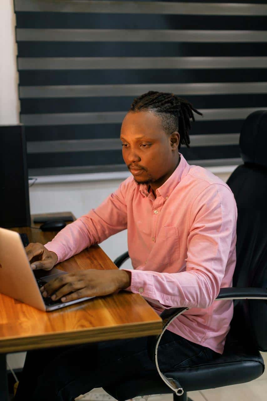 Software developer working on laptop in modern office with blinds